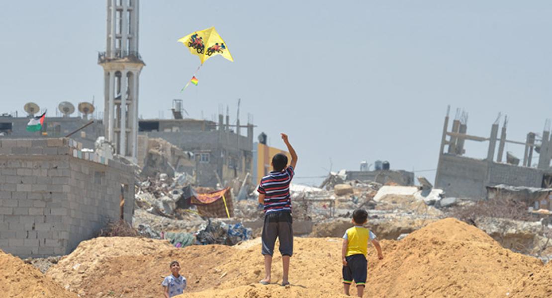 Boys flying a kite with rubble of buildings in background