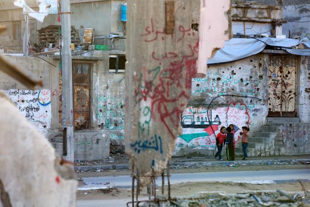 Children in Gaza play in front of ruined graffiti-covered buildings