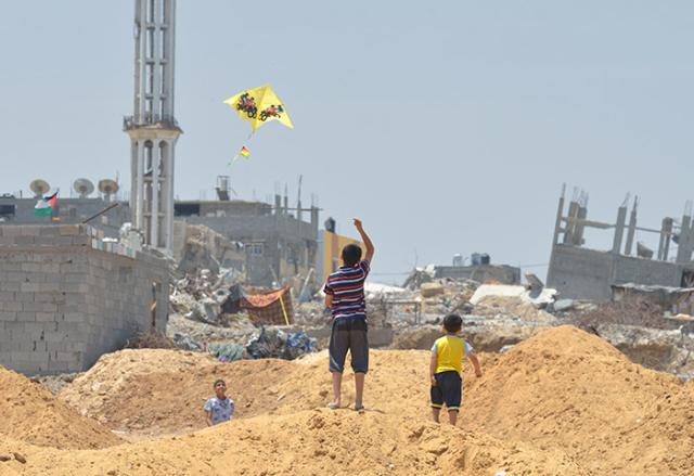 Boys flying a kite with rubble of buildings in background