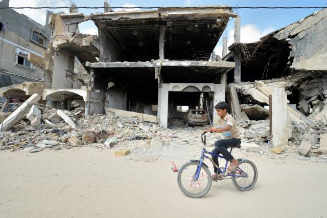 A boy rides a bike past ruined buildings in Khan Yunis
