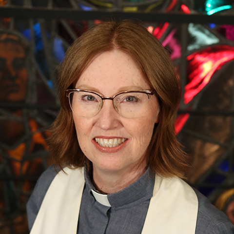 Rev. Kimberly Heath smiling, wearing a white stole and blue shirt with clerical colar