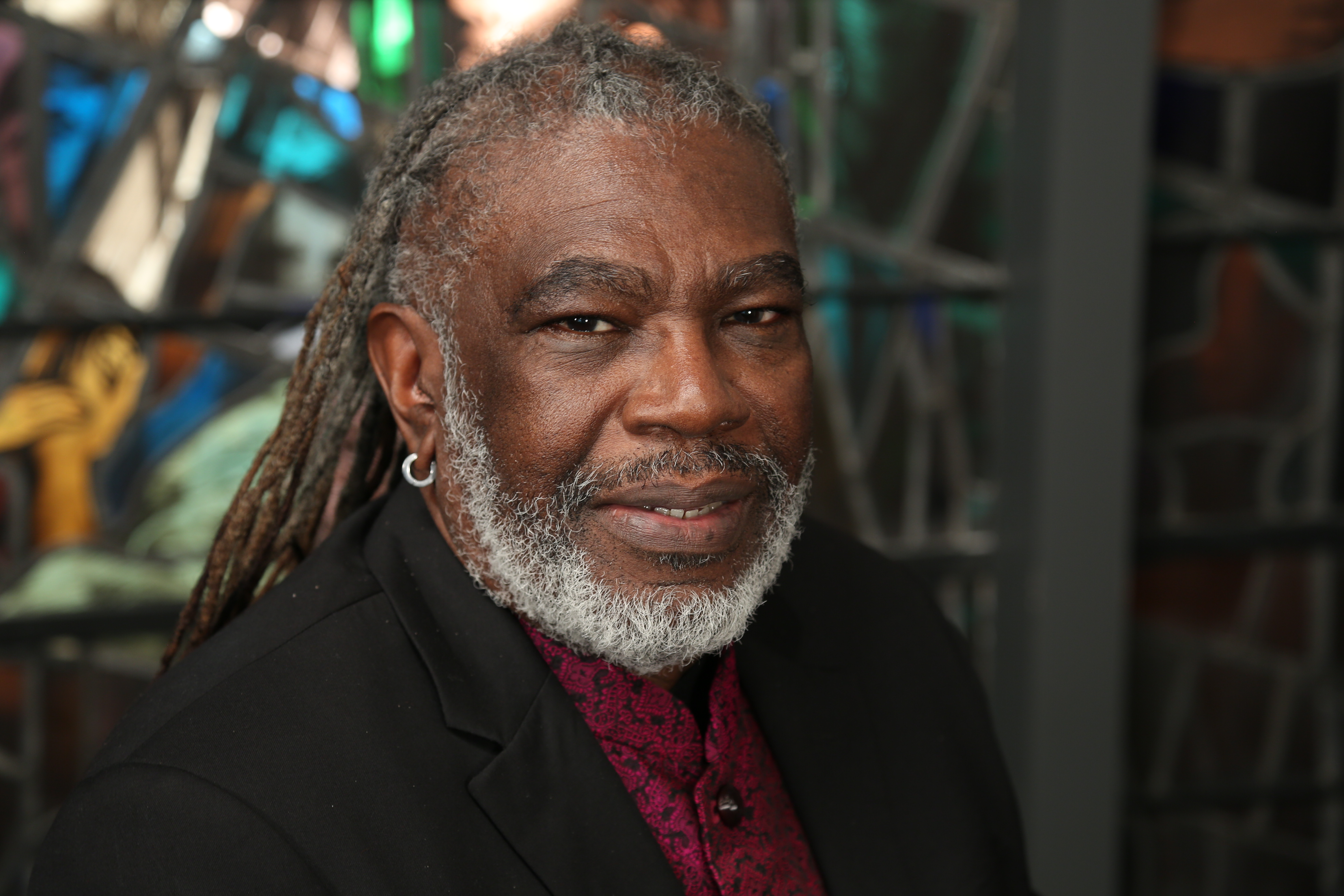 Michael Blair, a black man with a greying beard smiling in front of a stained glass window