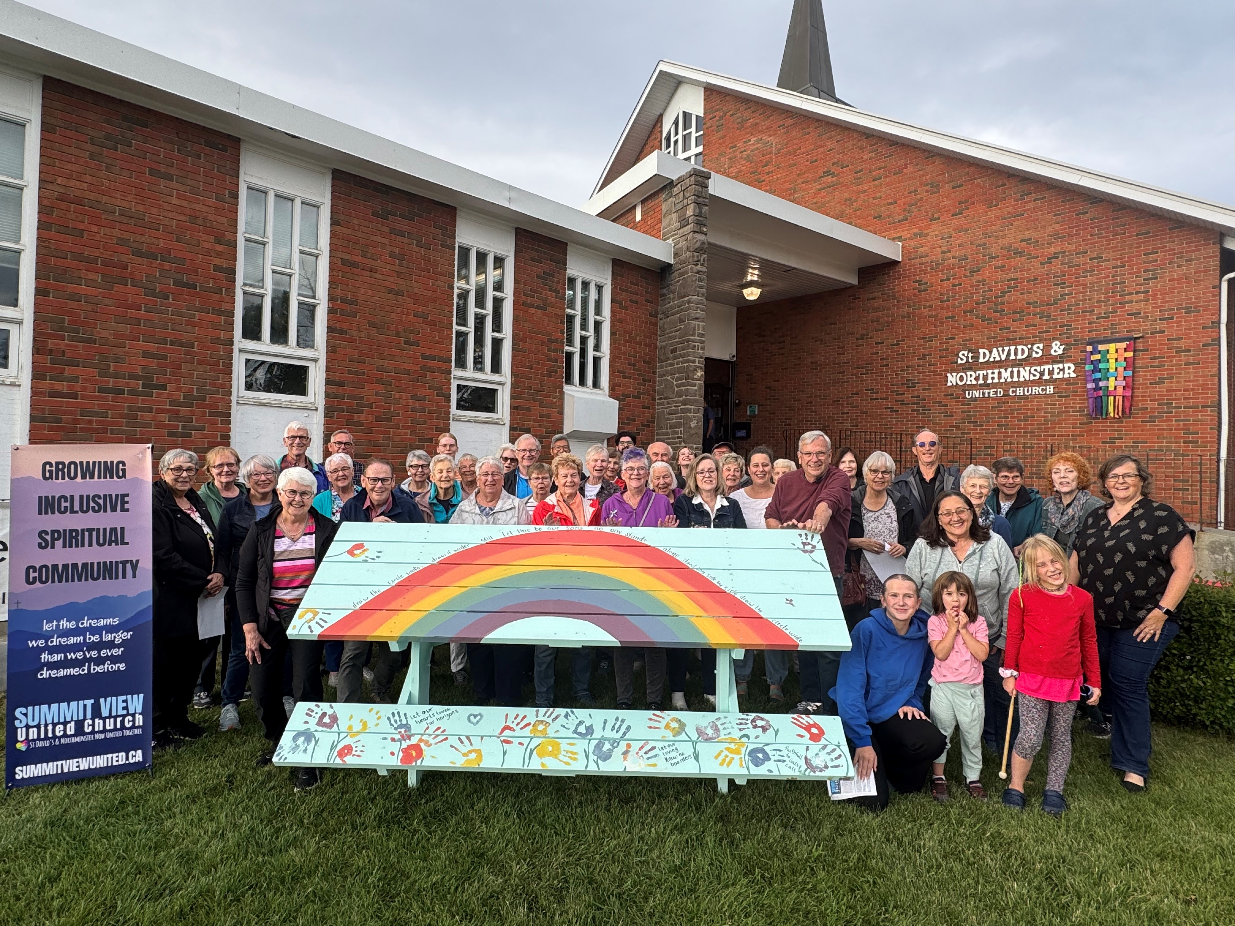 A large group of people standing behind a picnic table decorated for the 100 Tables project