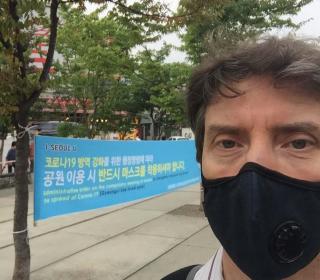 The author, John Egger, wears a pandemic face mask as he takes a selfie before a sign written in Korean in Seoul, Korea.