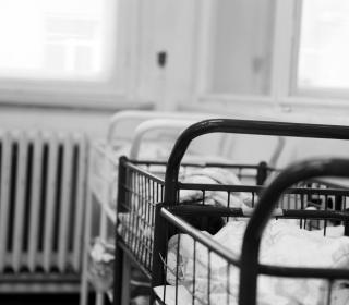 Rows of baby cradles covered with white sheets in this black and white archival photo from a maternity ward.