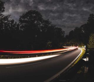 In a long exposure photo, headlights and taillights of cars blur as they rush around a corner at night.