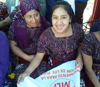 Two women in the traditional woven dress of women from Nebaj, Guatemala, show of some of the produce they grew using new agricultural skills.
