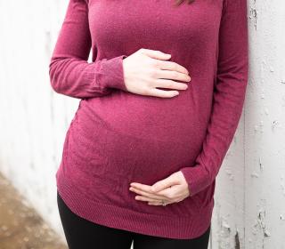 A pregnant woman in a red top standing next to a wooden fence.