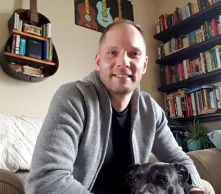 A photo of Jesse smiling in his home, with his dog.