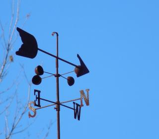 Metal weather vane made up of an arrow and north, south, east, west arrows against a blue sky