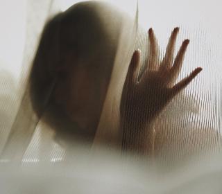 A woman's silhouetted face is mostly blurred by the curtain she's behind.