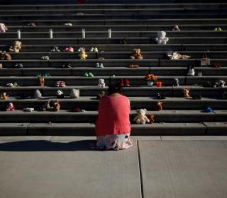 A woman dressed in orange kneels in front of the Victoria legislature steps, where children's shoes have been lined up.
