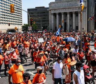 Rally participants hold up signs and wear orange shirts as they march down Portage Avenue, Winnipeg