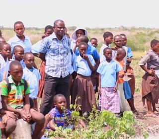 Emmanuel Baya stands in a Kenyan field surrounded by children.