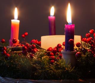 Coloured advent candles arranged in a pine wreath.