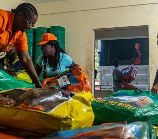 Two women in Haiti unload filled bags from the back of a pickup truck