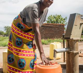 A woman in Africa fills a large orange water barrel from a tap