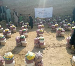 Afghan men and boys keep on eye on rows of bundles of food lined up on the ground in front of a wall.