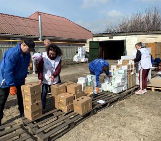 Aid workers load boxes of relief supplies onto pallets outdoors.