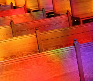 Rows of wooden pews with multicoloured light from stained glass reflected on them