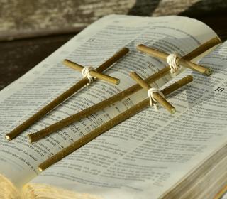 An open Bible with three crosses made of twigs lying across it.