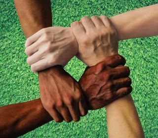Four hands in different skin colours are clasped at the wrists to form an interlocking square. 