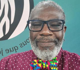 Michael Blair in a selfie wearing a maroon shirt with white dots and a jazzy multicoloured bowtie. A GC44 banner is in the background.