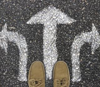 The viewer is looking down, at their feet, which at standing on a sign painted on the street with three arrows pointing in different directions.