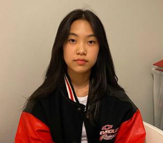 A Korean-Canadian teenage woman sitting and looking directly at the camera, wearing a red and black windbreaker.