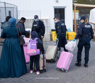 RCMP officers help a family of three asylum seekers, including a child, with their luggage at Roxham Road.