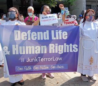 Several people at a protest hold up signs and a banner saying Defend Life & Human Rights