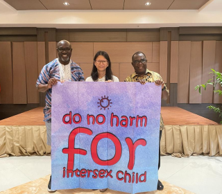 Three participants in the consultation hold a large pink sign saying "Do No Harm for Intersex Child"