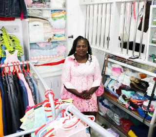A woman sits smiling in her clothing store surrounded by racks of clothes