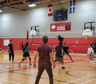 A group of young people from Madagascar playing volleyball in an indoor gym. Cameron Fraser is in the left corner, preparing to hit the ball