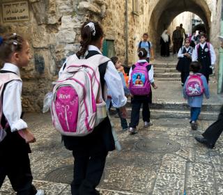 Palestinian children wearing backpacks walk to school
