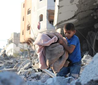 A child carrying a blanket walking through rubble in Gaza