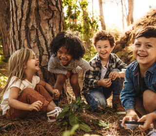 Four young children crouched under a tree are laughing.