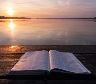 Open Bible lies on dock. The sun sets over a lake in the background.