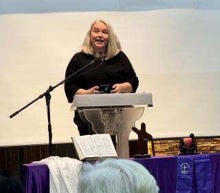 Emily Dwyer speaks at a podium that has an open Bible and cross in front of it.