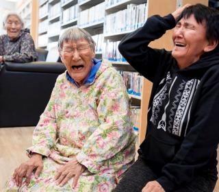 Two elderly Inuinnait women laugh along with a younger woman.