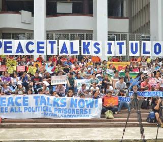 Large group of people hold up banners and signs urging peace talks in the Philippines.