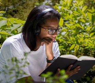 Young woman in white shirt reads a book outdoors, surrounded by trees.