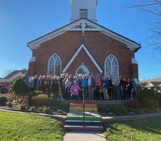 40 people in front of a church door with rainbow-painted steps.