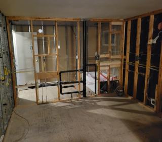 The interior of a house, stripped to the frames, with plumbing and electrical wires revealed.