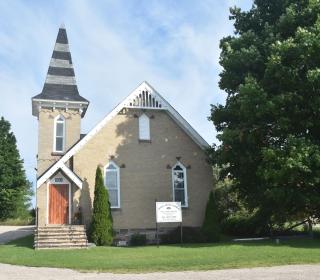 A small white church with a steeple, between two trees.
