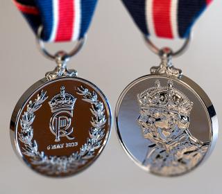 A photograph of both sides of a silver medal featuring the face of King Charles and the King's crest.
