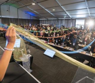A large room full of people holding ribbons together that reach across the room.