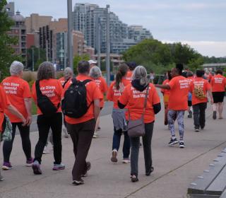 A group of people walking along a pathway wearing orange shirts.