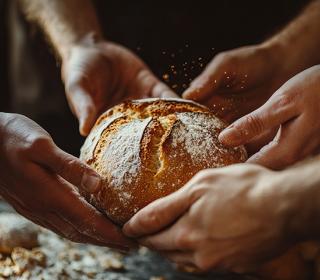 A boule of floured bread being shared with outreached hands