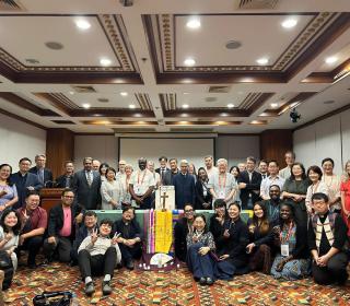 A large group photo in a conference room with several subject wearing religious garments.